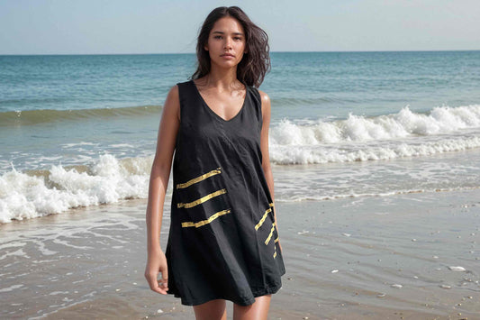 Frau im schwarzen Sommerkleid mit goldenen Siebdruckstreifen läuft am Strand entlang