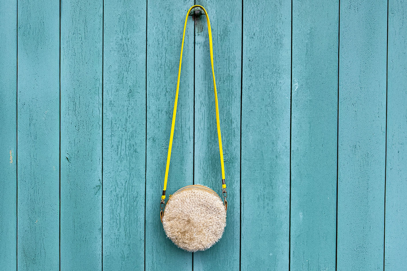 Runde Umhängetasche Peppa vor blauem Hintergrund. Tasche besteht aus upcycled Materialien mit gehäkeltem Deckel in der Farbe gold.