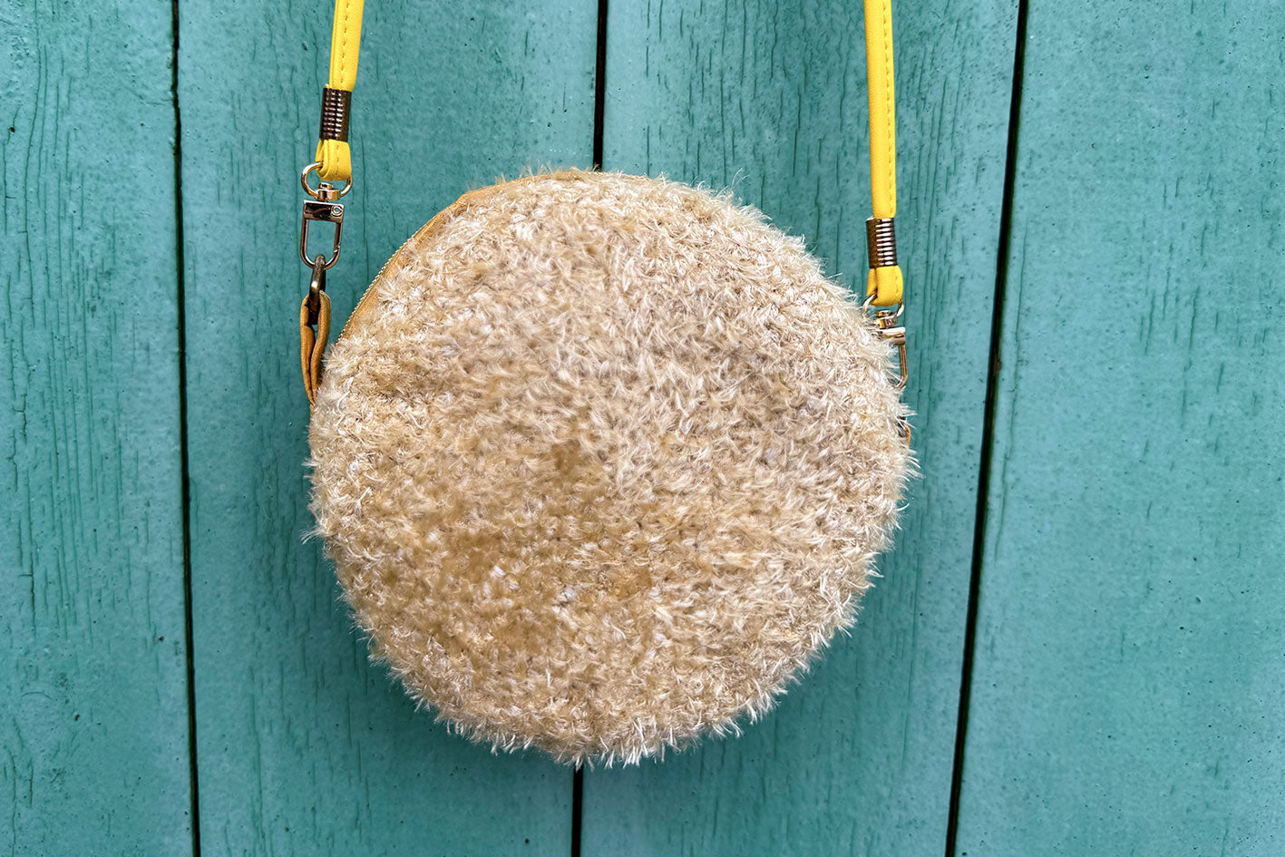 Runde Umhängetasche Peppa vor blauem Hintergrund. Tasche besteht aus upcycled Materialien mit gehäkeltem Deckel in der Farbe gold.