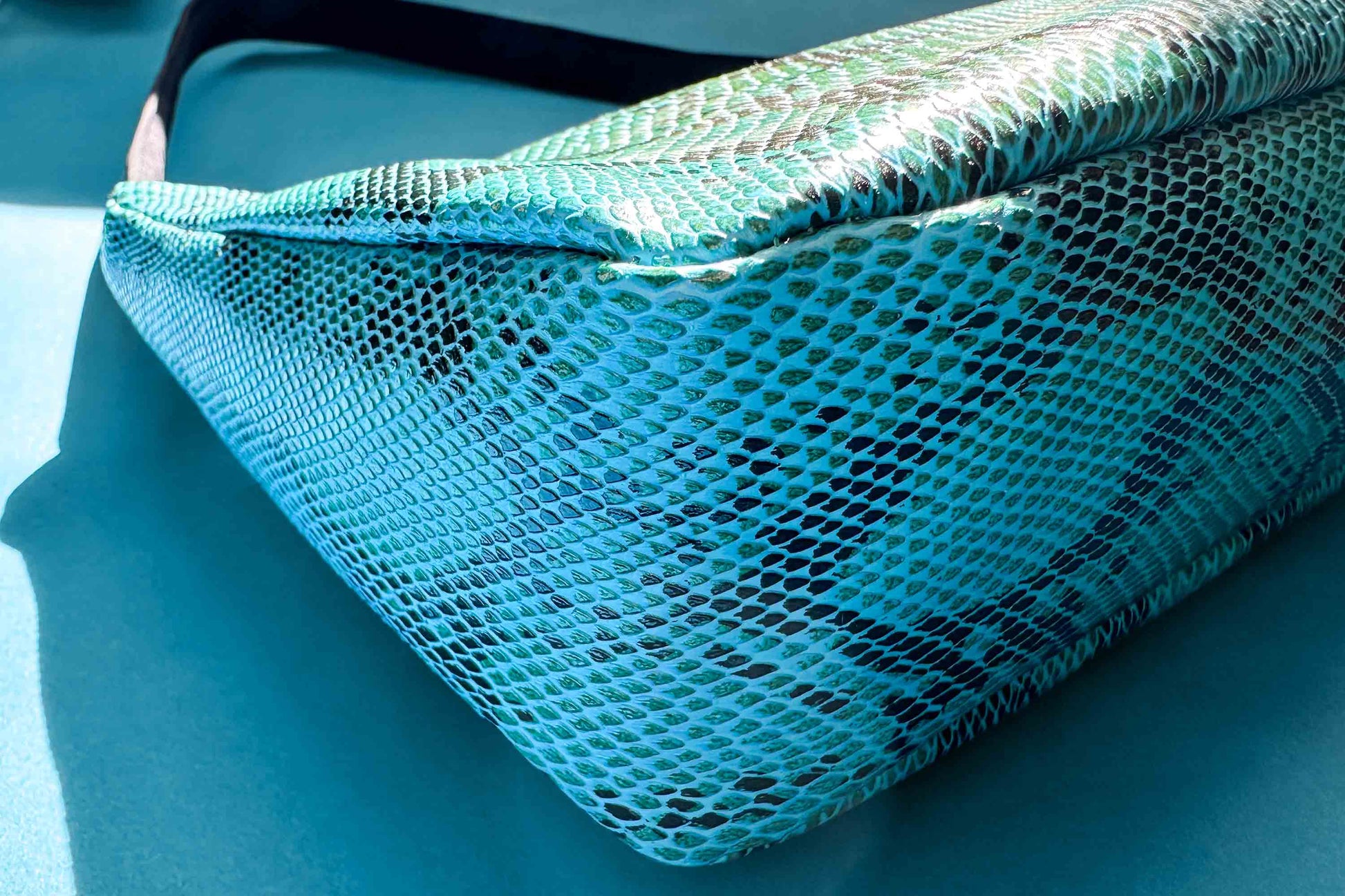 Detailansicht blaue Schultertasche in Schlangeleder Optik vor blauem Hintergrund mit schwarzem Gurtband. Hergestellt aus upcycled Materialien von Jeff Every Piece A Friend.