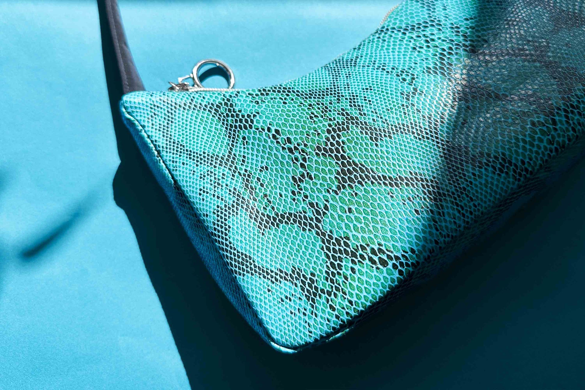 Detailansicht blaue Schultertasche in Schlangeleder Optik vor blauem Hintergrund mit schwarzem Gurtband und silbernen Reißverschluss. Hergestellt aus upcycled Materialien von Jeff Every Piece A Friend.