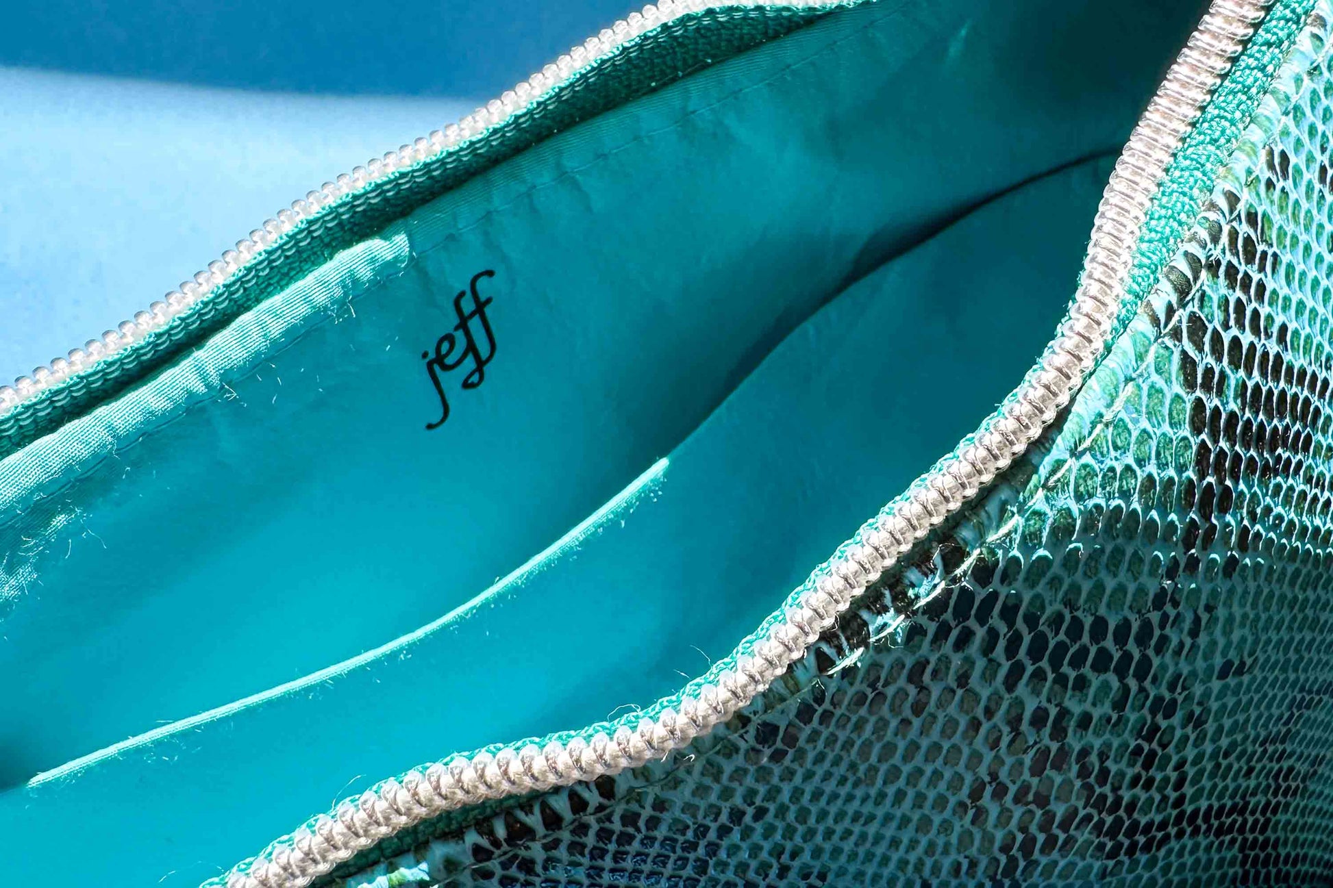 Detailansicht von Innenfach. Blaue Schultertasche in Schlangeleder Optik vor blauem Hintergrund mit schwarzem Gurtband und silbernen Reißverschluss. Hergestellt aus upcycled Materialien von Jeff Every Piece A Friend.