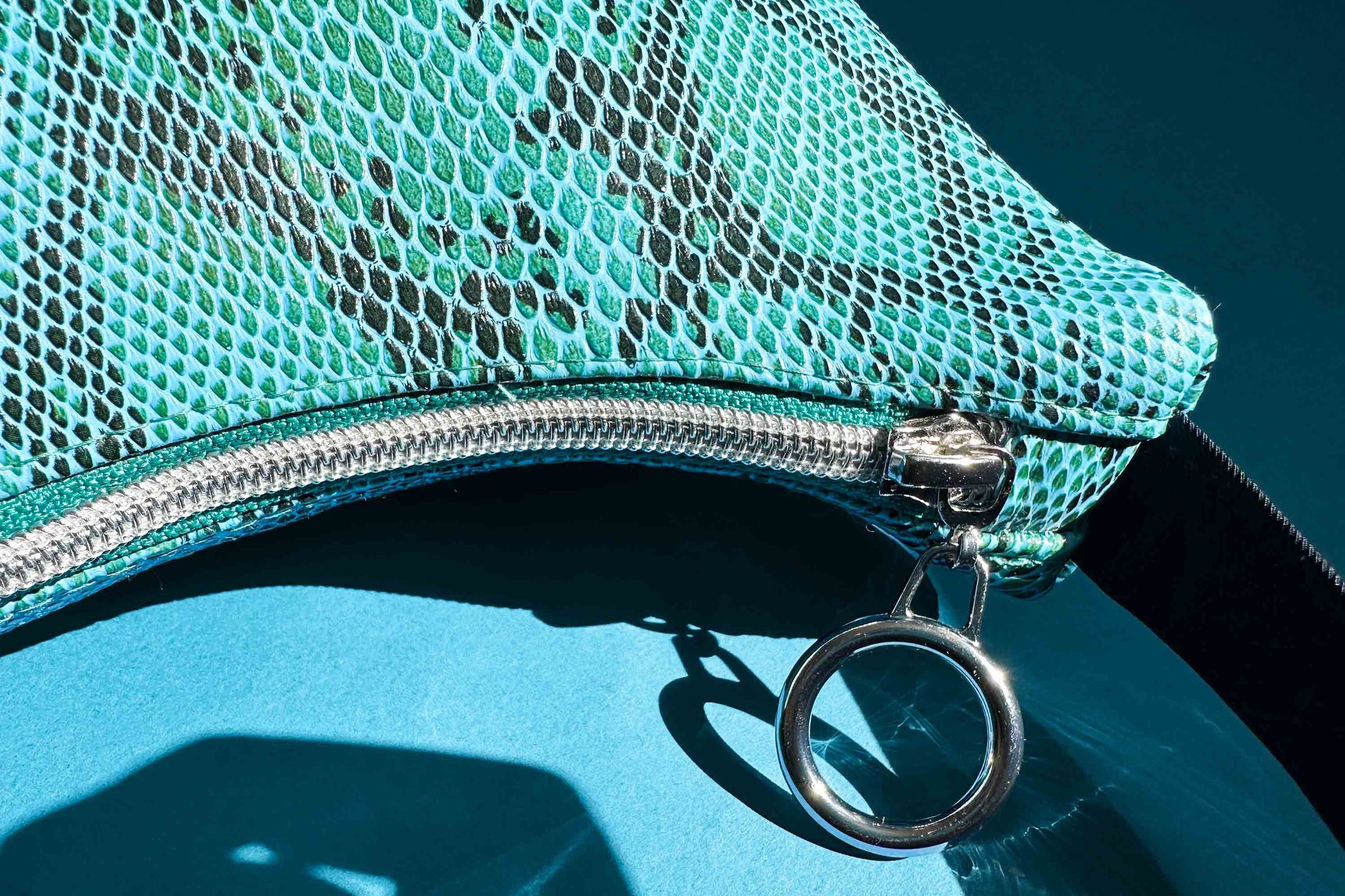 Detailansicht blaue Schultertasche in Schlangeleder Optik vor blauem Hintergrund mit schwarzem Gurtband und silbernen Reißverschluss. Hergestellt aus upcycled Materialien von Jeff Every Piece A Friend.