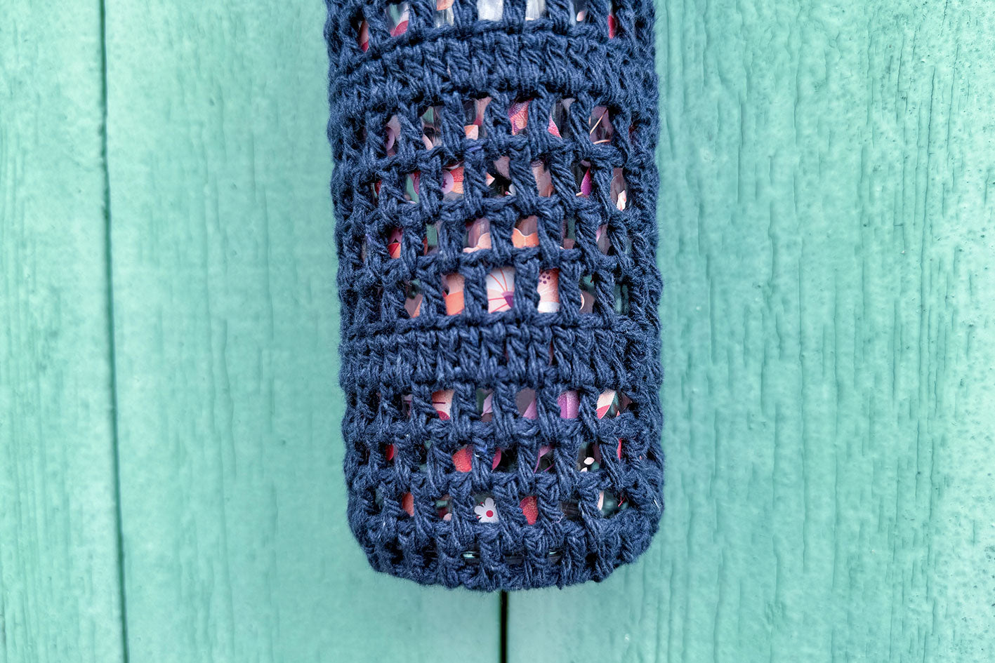 Detailansicht: Gehäkelter, dunkelblauer Flaschenhalter CHRISTA von Jeff Every Piece A Friend vor blauem Hintergrund.