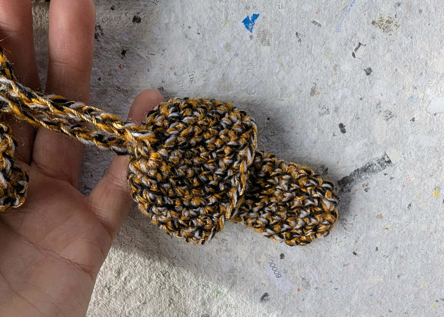 Hand mit gelb-schwarz gehäkeltem Feuerzeughalter zum Umhängen in Fliegenpilzoptik