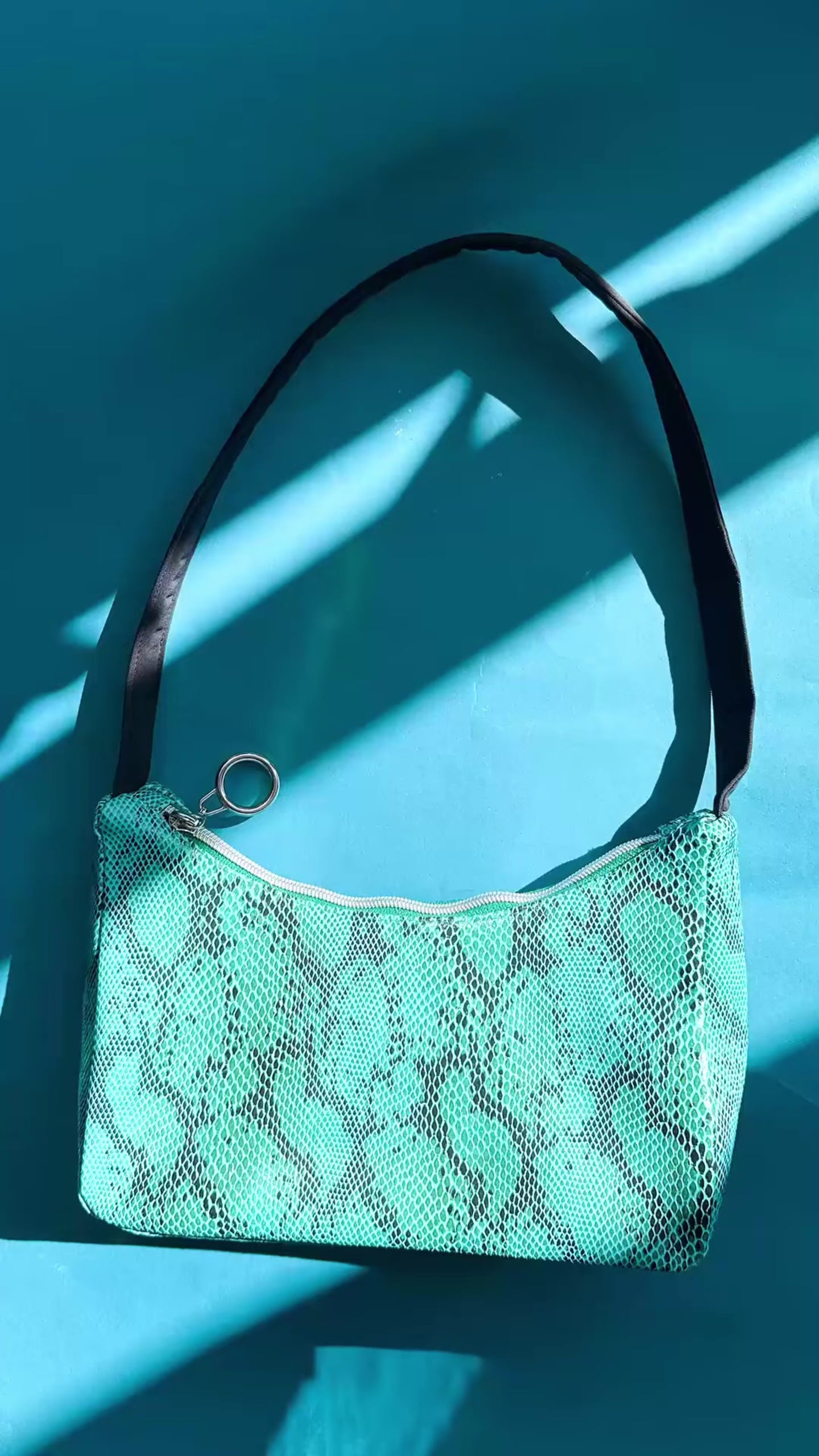 Video: Gesamtansicht blaue Schultertasche in Schlangeleder Optik vor blauem Hintergrund mit schwarzem Gurtband. Hergestellt aus upcycled Materialien von Jeff Every Piece A Friend.