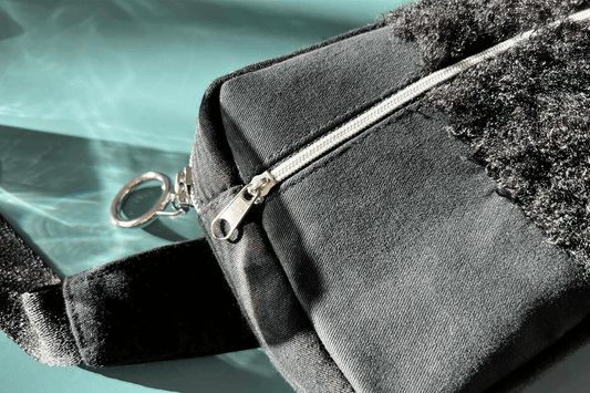 Detailansicht Bauchtasche aus Upclycling-Materialien mit silbernem Reißverschluss vor blauem Hintergrund.