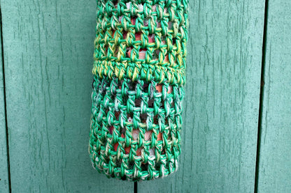 Detailansicht: Gehäkelter, Flaschenhalter CHRISTA von Jeff Every Piece A Friend vor blauem Hintergrund. Der Flaschenhalter ist aus Baumwolle und kommt in verschiedenen Grüntönen. 