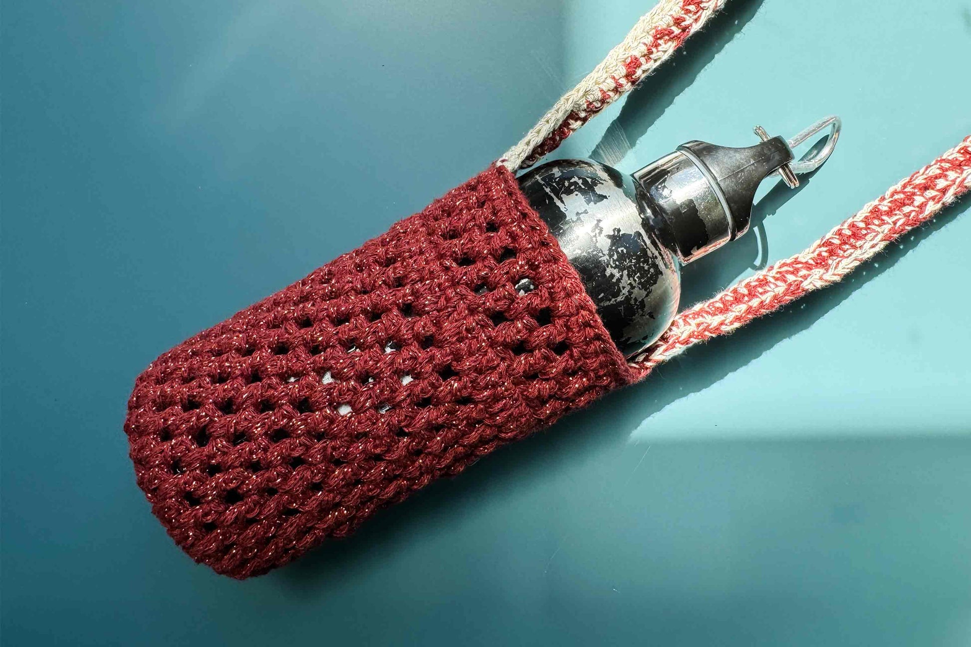 Detailansicht des gehäkelten, rot-beige glitzernden Flaschenhalters zum Umhängen CHRISTA mit Trinkflasche 