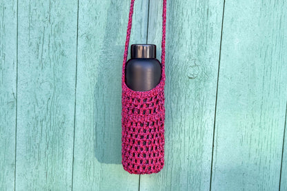 Gehäkelter, Flaschenhalter CHRISTA von Jeff Every Piece A Friend vor blauem Hintergrund. Der Flaschenhalter hat die Farbe pink oder magenta gemischt.