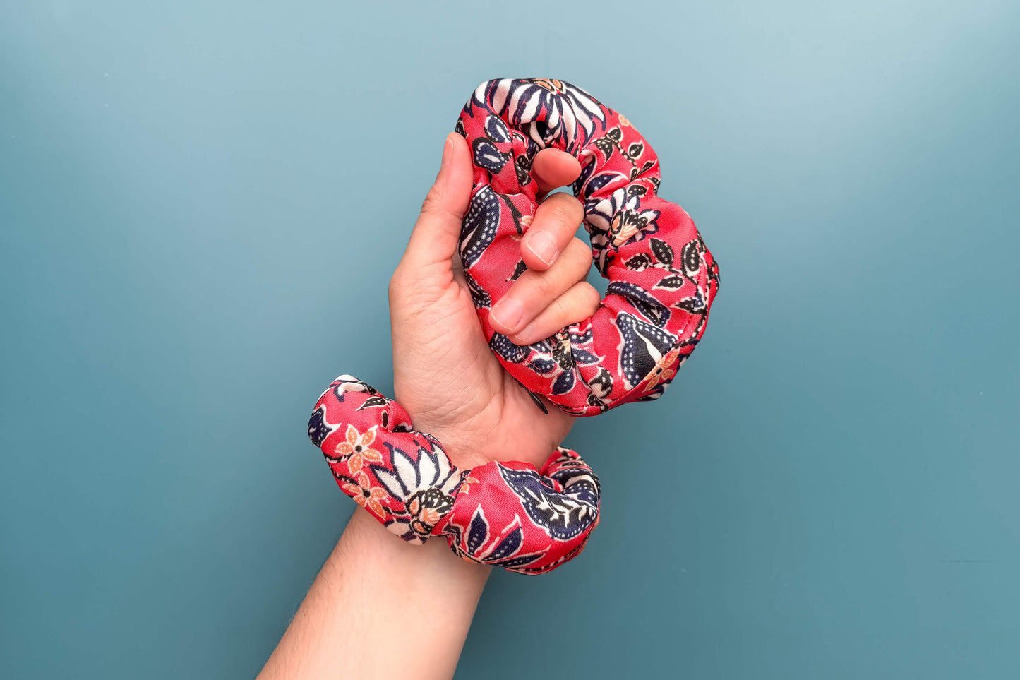 Eine Hand trägt zwei altrosa Scrunchies mit Reißverschluss und weiß-schwarz-orangem Blumenmuster.  Jeff - everyPieceAFriend