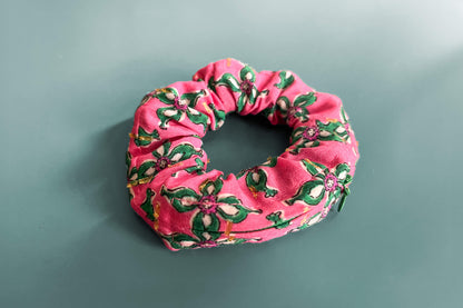 Ansicht von oben: Ein Scrunchie mit Reißverschluss und einem Blumenmuster in roten und grünen Tönen liegt auf einem blauen Tisch. Der Reißverschluss ist geschlossen.