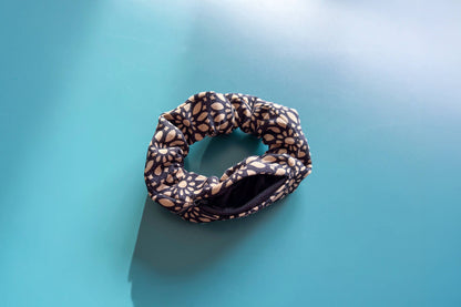 Ansicht von oben: Ein Scrunchie mit Reißverschluss und schwarz-beigen Blumenmuster liegt auf einem blauen Tisch. Der Reißverschluss ist geöffnet.