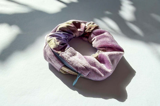 Ansicht von schräg oben: ein lila-bunt gemusterter Scrunchie mit einem hellblauen Reißverschluss liegt auf einem weißen Hintergrund. jeff - everypieceafriend