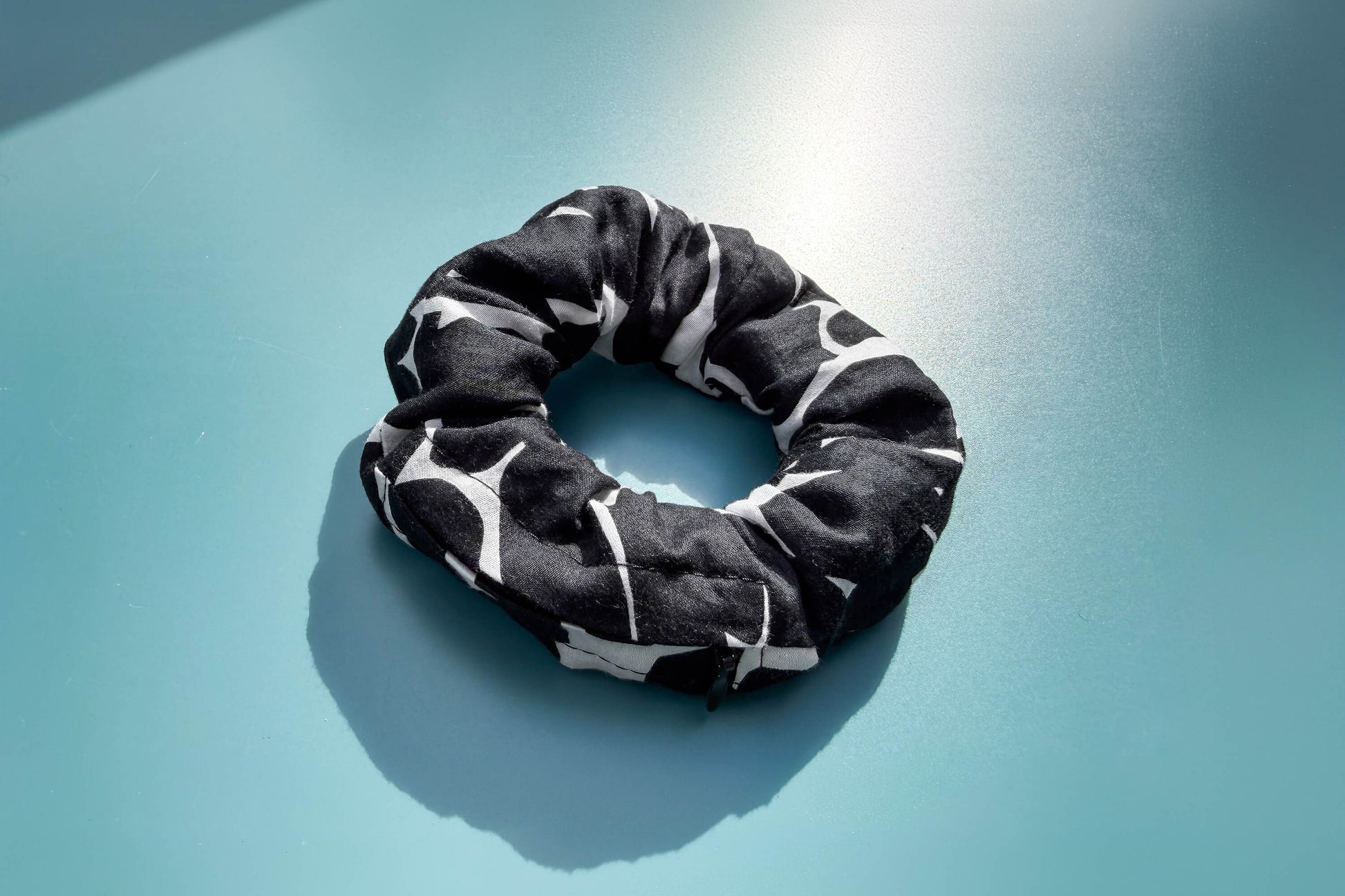 Ansicht von oben: Ein schwarz-weißer Scrunchie mit schwarzen Reißverschluss liegt auf einem blauen Tisch. Der Reißverschluss ist geschlossen.  Jeff - EveryPieceAFriend