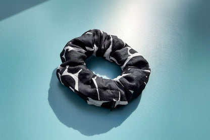 Ansicht von oben: Ein schwarz-weißer Scrunchie mit schwarzen Reißverschluss liegt auf einem blauen Tisch. Der Reißverschluss ist geschlossen.  Jeff - EveryPieceAFriend