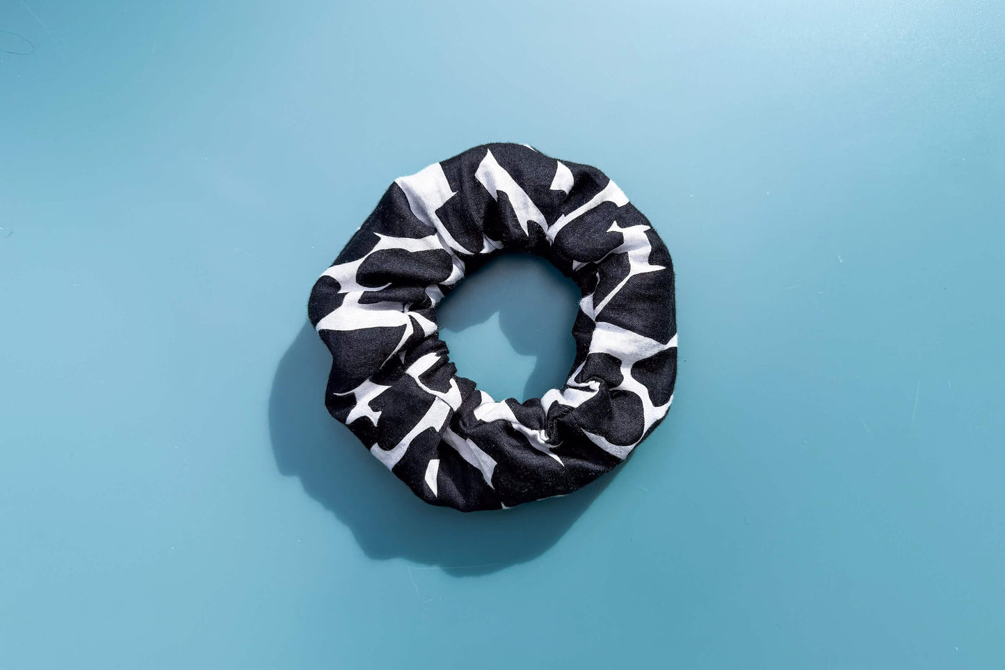 Ansicht von oben: Ein schwarz-weißer Scrunchie mit schwarzen Reißverschluss liegt auf einem blauen Tisch. Der Reißverschluss ist geschlossen.  Jeff - EveryPieceAFriend