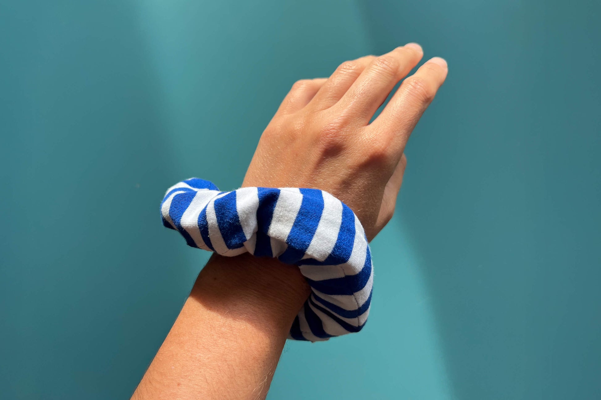Eine Hand trägt einen dunkelblau-weißen gestreiften Scrunchie am Handgelenk vor blauem Hintergrund. Der Scrunchie besteht aus upcycled Materialien und hat einen weißen Reißverschluss.