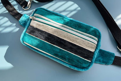 Gesamtansicht einer Bauchtasche aus Samt von Jeff EveryPieceAFriend. Die Tasche ist blau und grau gestreift, hat ein schwarzes Gurtband und einen silbernen Reißverschluss. 