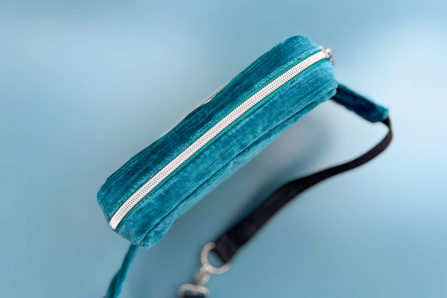 Gesamtansicht von oben einer Bauchtasche aus Samt von Jeff EveryPieceAFriend. Die Tasche ist blau und grau gestreift, hat ein schwarzes Gurtband und einen silbernen Reißverschluss. 