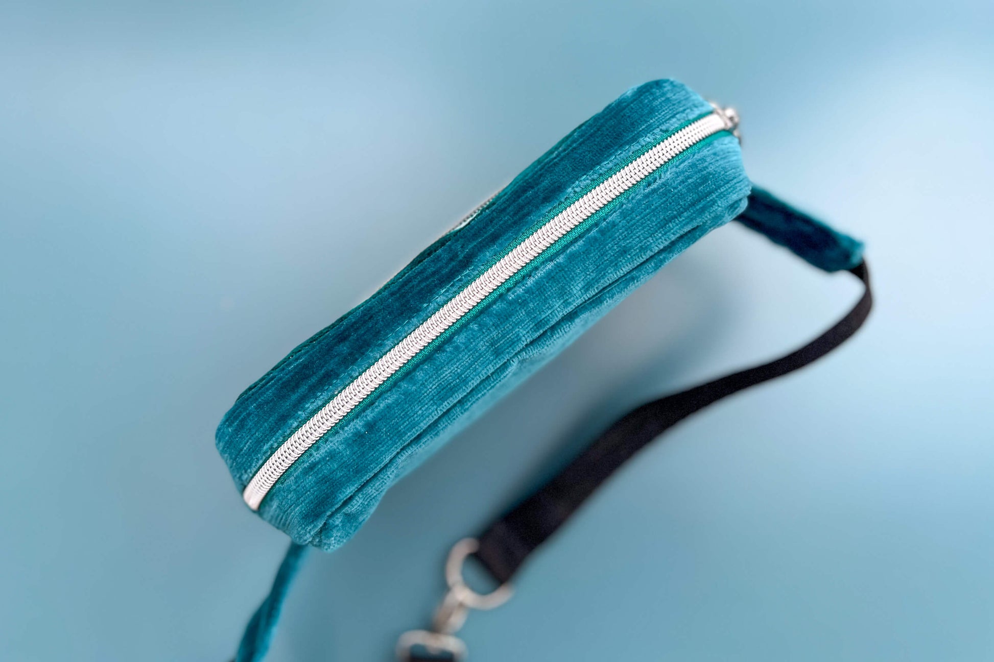 Gesamtansicht von oben einer Bauchtasche aus Samt von Jeff EveryPieceAFriend. Die Tasche ist blau und grau gestreift, hat ein schwarzes Gurtband und einen silbernen Reißverschluss. 