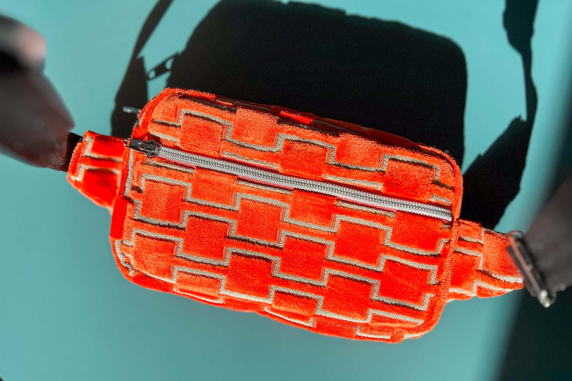 Gesamtansicht einer Bauchtasche aus upcycled Möbelstoff von Jeff EveryPieceAFriend. Die Tasche ist orange gemustert, hat ein schwarzes Gurtband und einen silbernen Reißverschluss.
