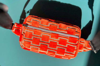 Gesamtansicht einer Bauchtasche aus upcycled Möbelstoff von Jeff EveryPieceAFriend. Die Tasche ist orange gemustert, hat ein schwarzes Gurtband und einen silbernen Reißverschluss.