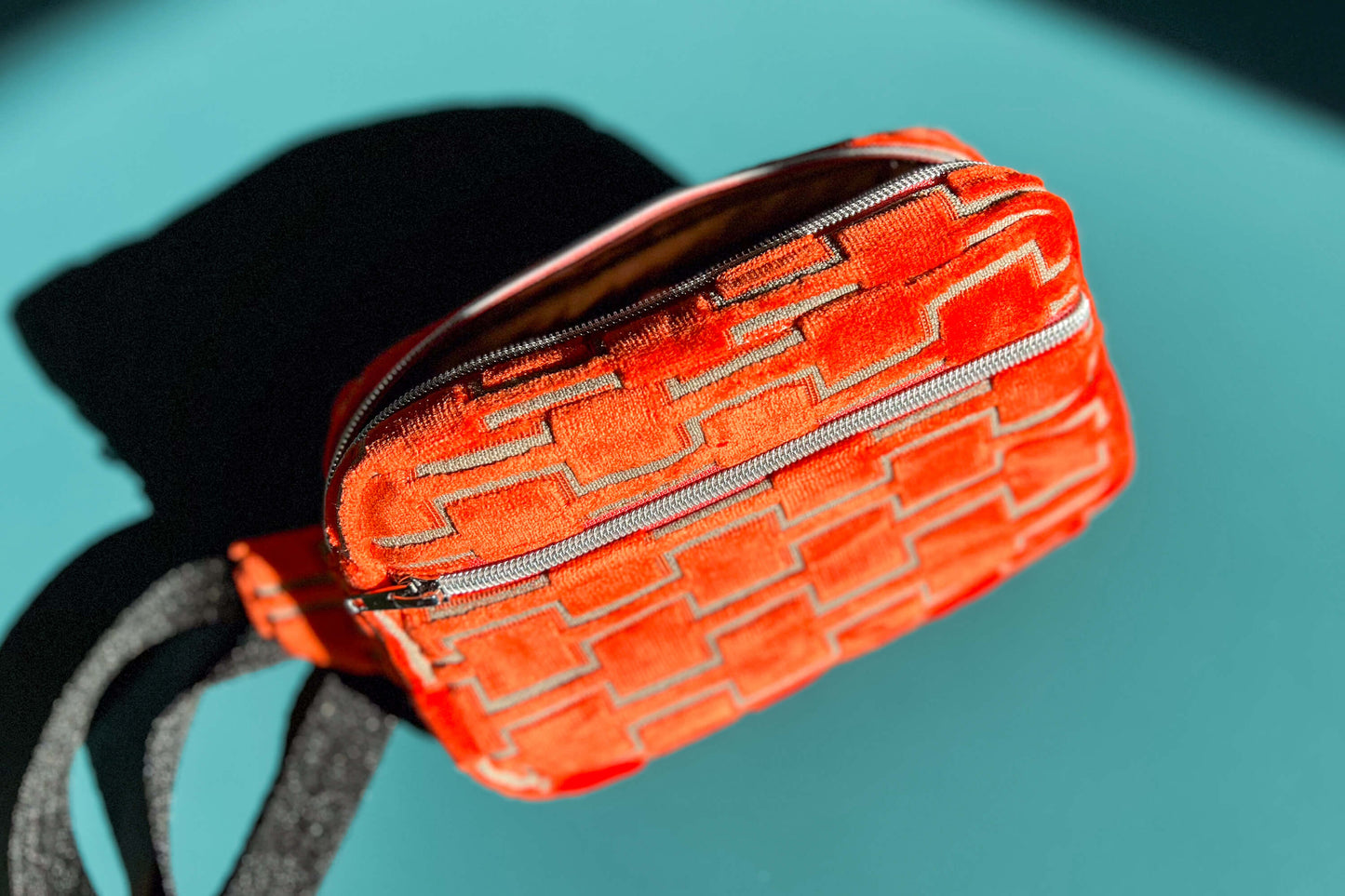 Gesamtansicht einer Bauchtasche aus upcycled Möbelstoff von Jeff EveryPieceAFriend. Die Tasche ist orange gemustert, hat ein schwarzes Gurtband und einen silbernen Reißverschluss.