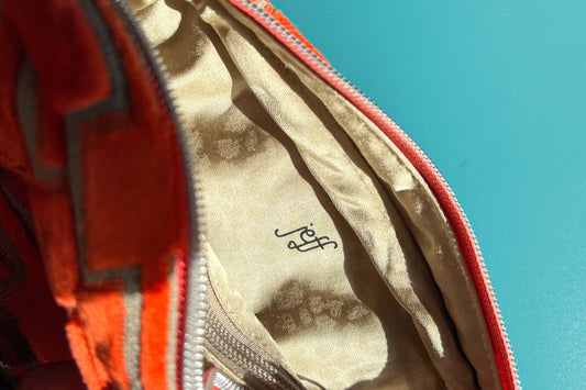 Detailansicht einer geöffneten Bauchtasche aus upcycled Möbelstoff von Jeff EveryPieceAFriend. Die Tasche ist orange gemustert, hat ein schwarzes Gurtband und einen silbernen Reißverschluss. Das Innenfach der Tasche ist beige.