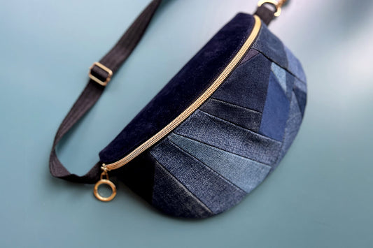 Gesamtansicht von großer Bauchtasche aus upcycled Denim im Patchwork Look. Die Tasche hat einen goldenen Reißverschluss und ein schwarzes Gurtband.