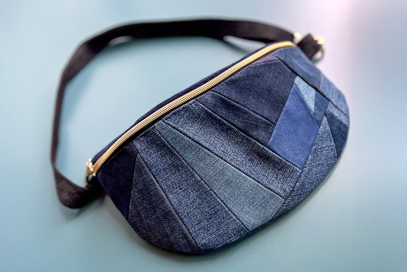 Gesamtansicht von großer Bauchtasche aus upcycled Denim im Patchwork Look. Die Tasche hat einen goldenen Reißverschluss und ein schwarzes Gurtband.