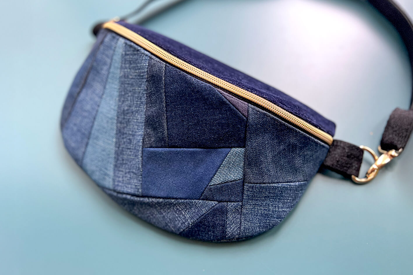 Gesamtansicht von großer Bauchtasche aus upcycled Denim im Patchwork Look. Die Tasche hat einen goldenen Reißverschluss und ein schwarzes Gurtband.