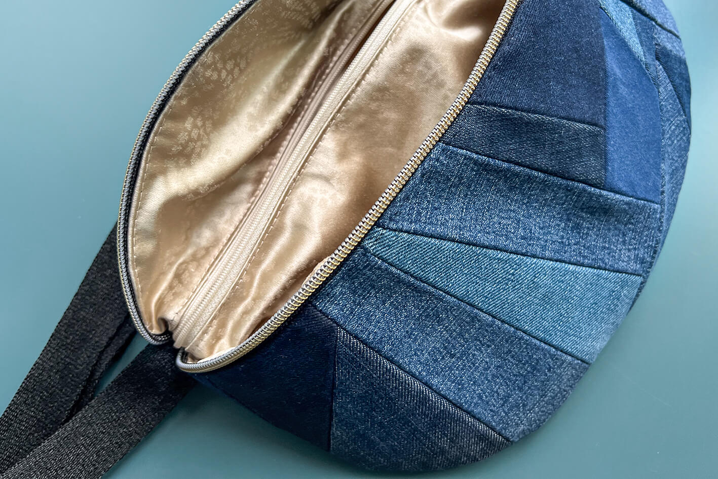 Detailansicht von großer Bauchtasche aus upcycled Denim im Patchwork Look. Die Tasche ist geöffnet und das Bild zeigt das Innenfach in der Farbe gold.