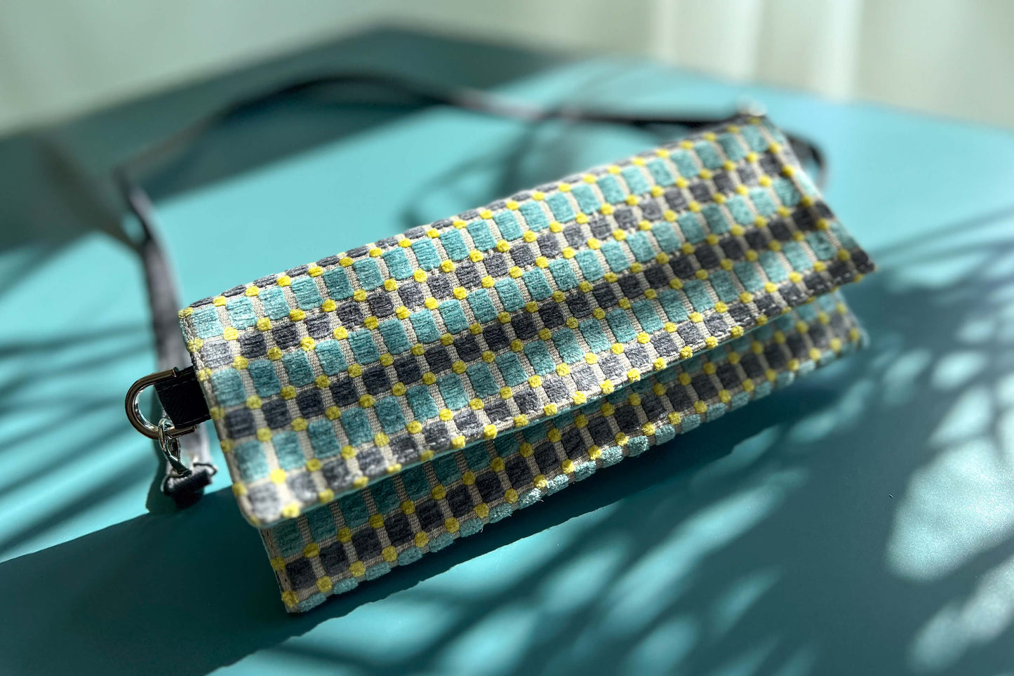 Gesamtansicht der kleinen Umhängetasche DANA aus upcycled Polsterstoff in den Farben blau, gelb und beige mit silbernen Verschlüssen. 