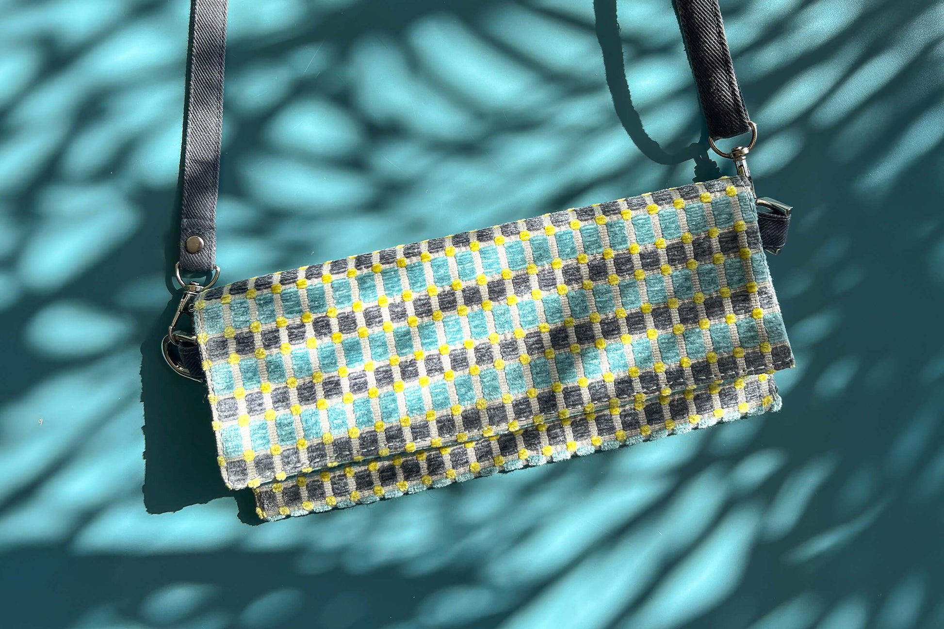 Gesamtansicht der kleinen Umhängetasche DANA aus upcycled Polsterstoff in den Farben blau, gelb und beige mit silbernen Verschlüssen. 