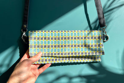 Gesamtansicht: Hand hält die Umhängetasche DANA aus upcycled Polsterstoff in den Farben blau, gelb und beige mit silbernen Verschlüssen in die Kamera. 