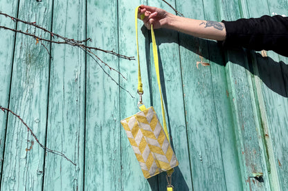 Gesamtansicht: Hand hält Umhängetasche DANA aus upcycled gold-silbernen Polsterstoff vor blauem Hintergrund ins Bild.
