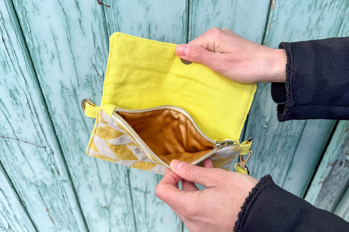 Gesamtansicht: Hand hält Umhängetasche DANA aus upcycled gold-silbernen Polsterstoff vor blauem Hintergrund ins Bild.