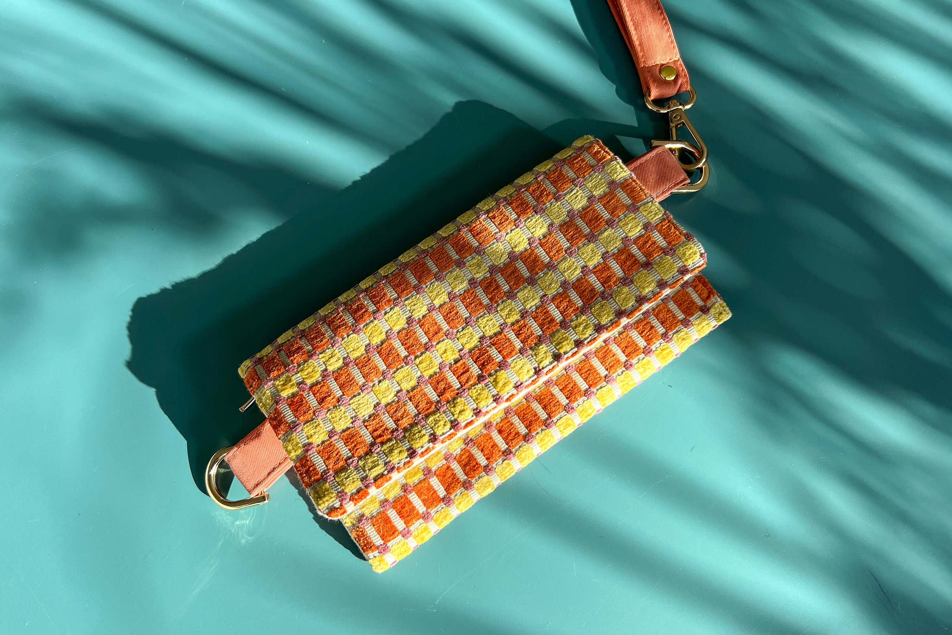 Gesamtansicht der Handtasche DANA in der Farbe gelb-orange-beige. Die Tasche liegt auf einem blauen Untergrund.