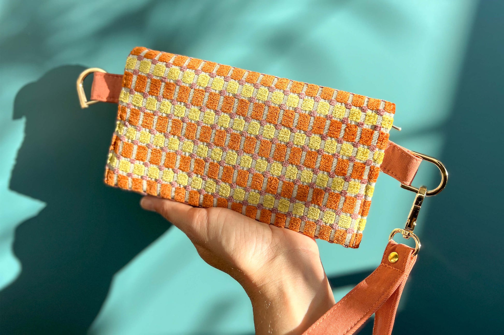 Gesamtansicht der Rückseite Handtasche DANA in der Farbe gelb-orange-beige. Die Tasche liegt auf einem blauen Untergrund.