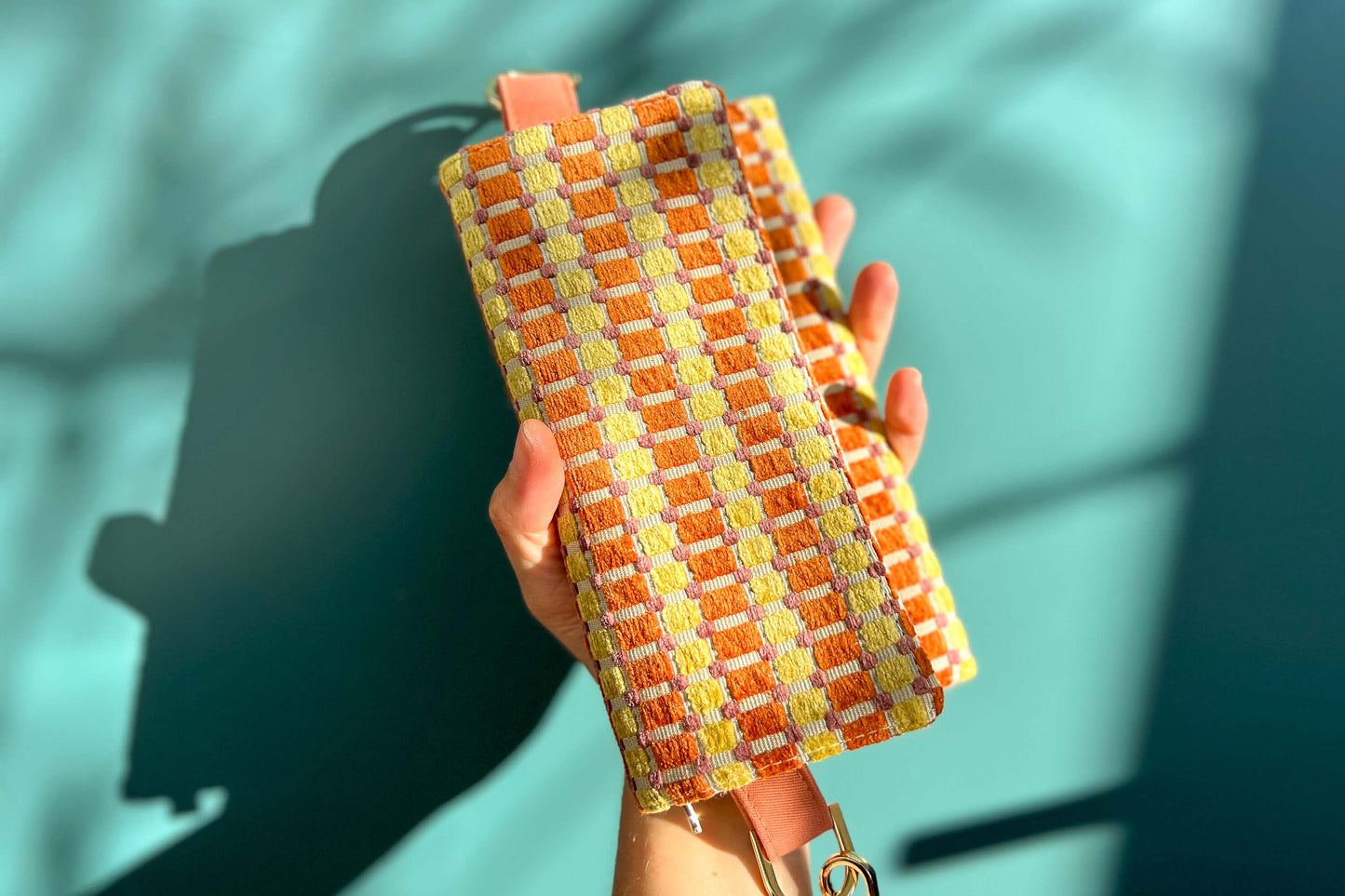 Gesamtansicht der Handtasche DANA in der Farbe gelb-orange-beige. Die Tasche liegt auf einem blauen Untergrund.