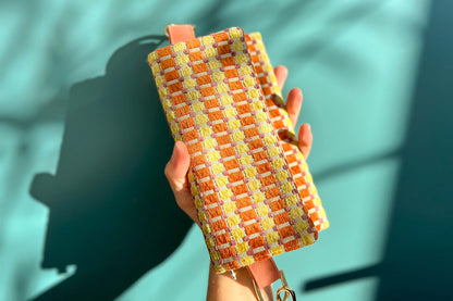 Gesamtansicht der Handtasche DANA in der Farbe gelb-orange-beige. Die Tasche liegt auf einem blauen Untergrund.