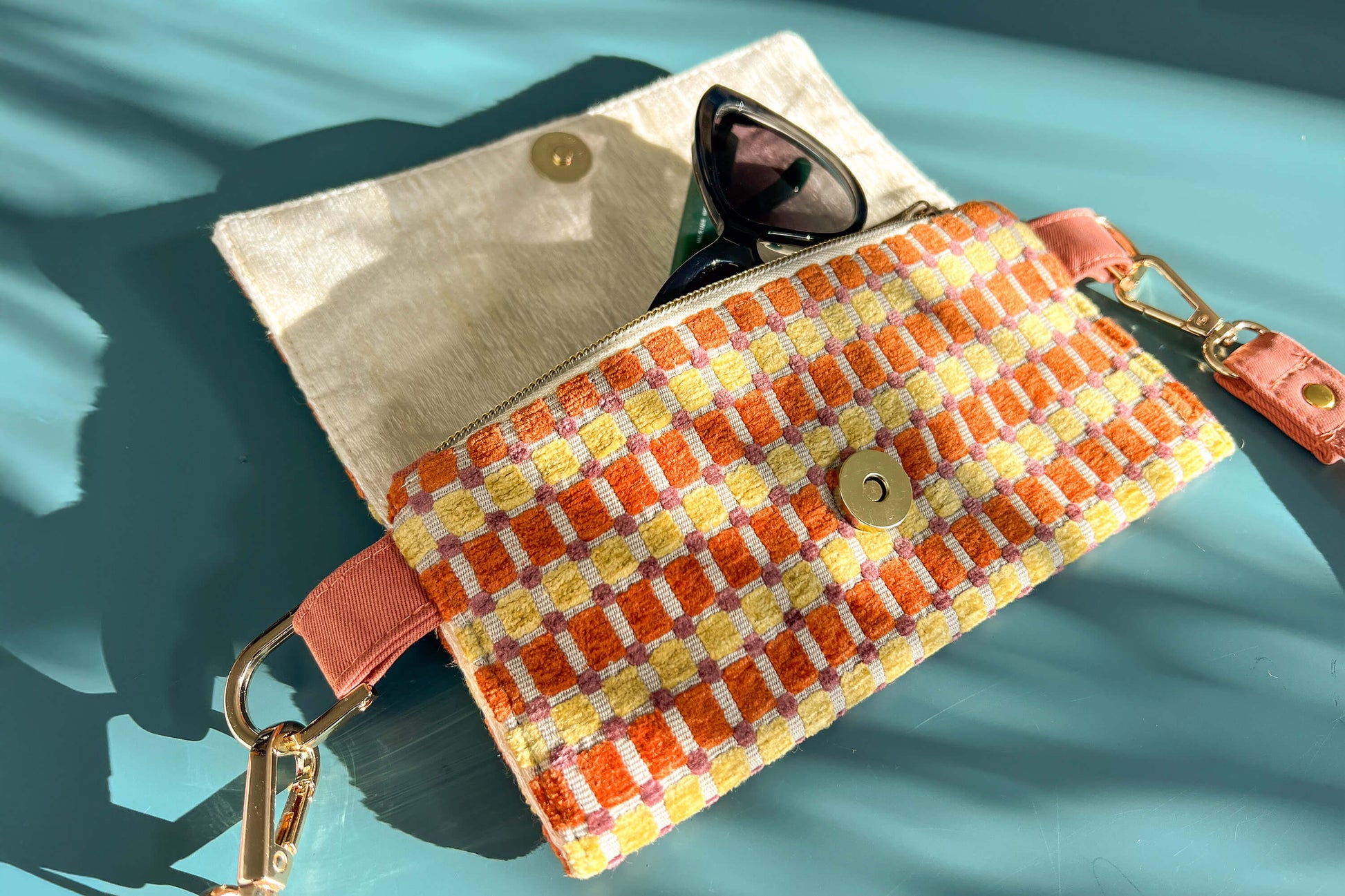 Gesamtansicht der geöffneten Handtasche DANA in der Farbe gelb-orange-beige. Die Tasche liegt auf einem blauen Untergrund.