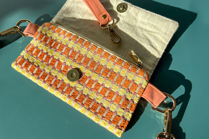 Gesamtansicht der Handtasche DANA in der Farbe gelb-orange-beige. Die Tasche liegt auf einem blauen Untergrund.