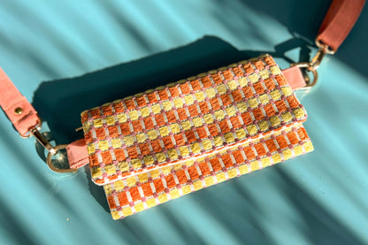 Gesamtansicht der Handtasche DANA in der Farbe gelb-orange-beige. Die Tasche liegt auf einem blauen Untergrund.