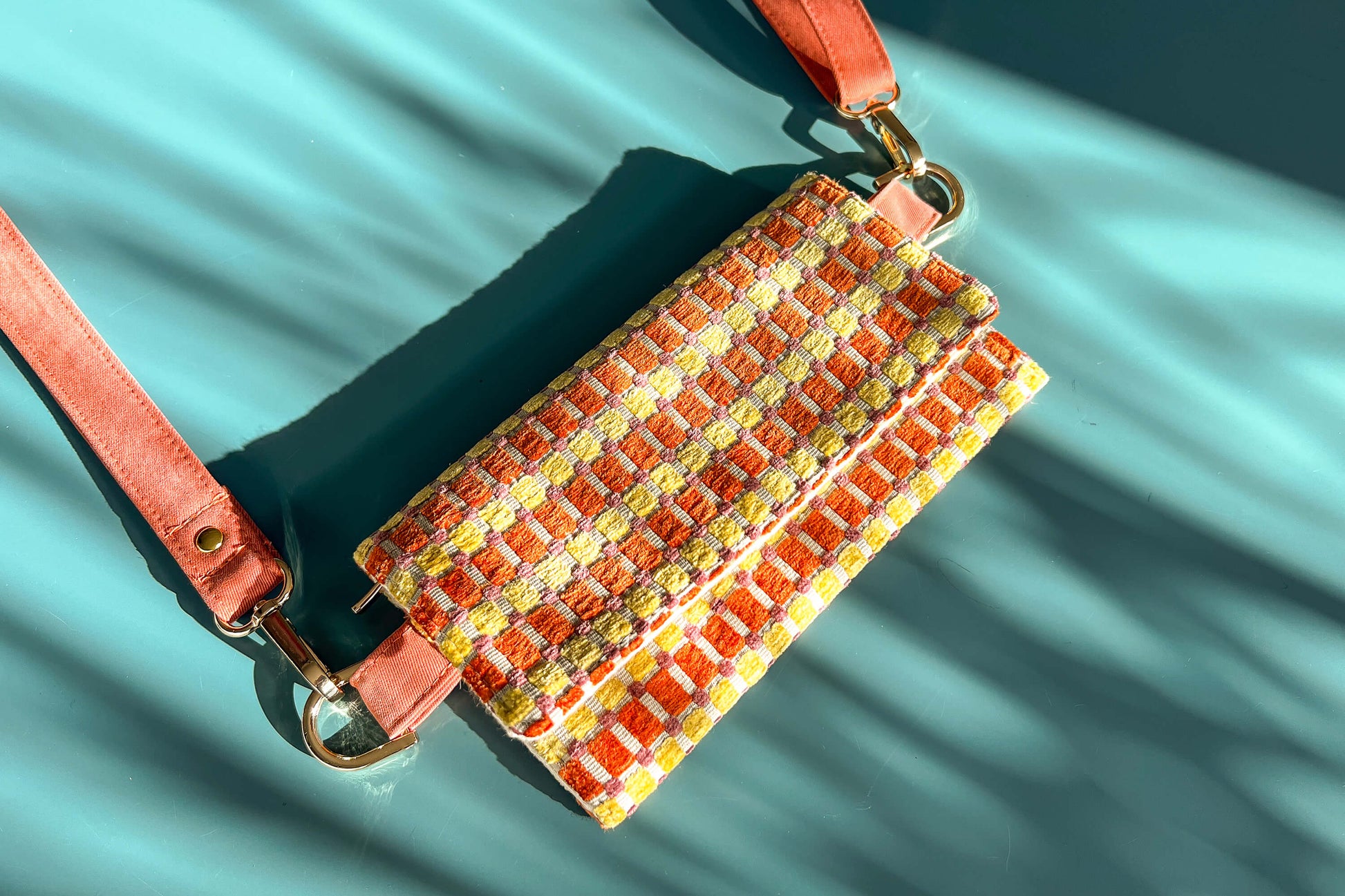 Gesamtansicht der Handtasche DANA in der Farbe gelb-orange-beige. Die Tasche liegt auf einem blauen Untergrund.