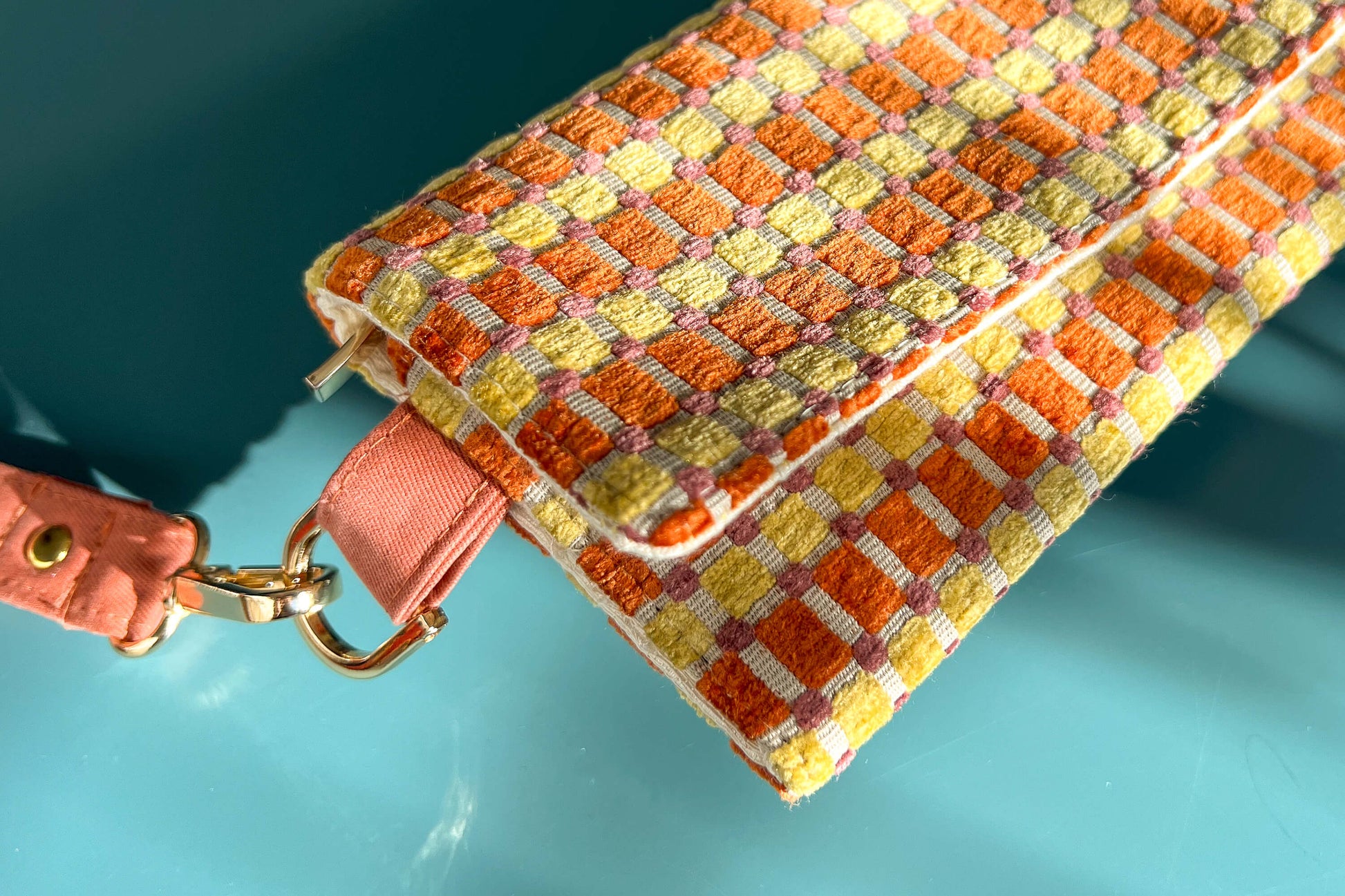 Detailnsicht der Handtasche DANA in der Farbe gelb-orange-beige. Die Tasche liegt auf einem blauen Untergrund.