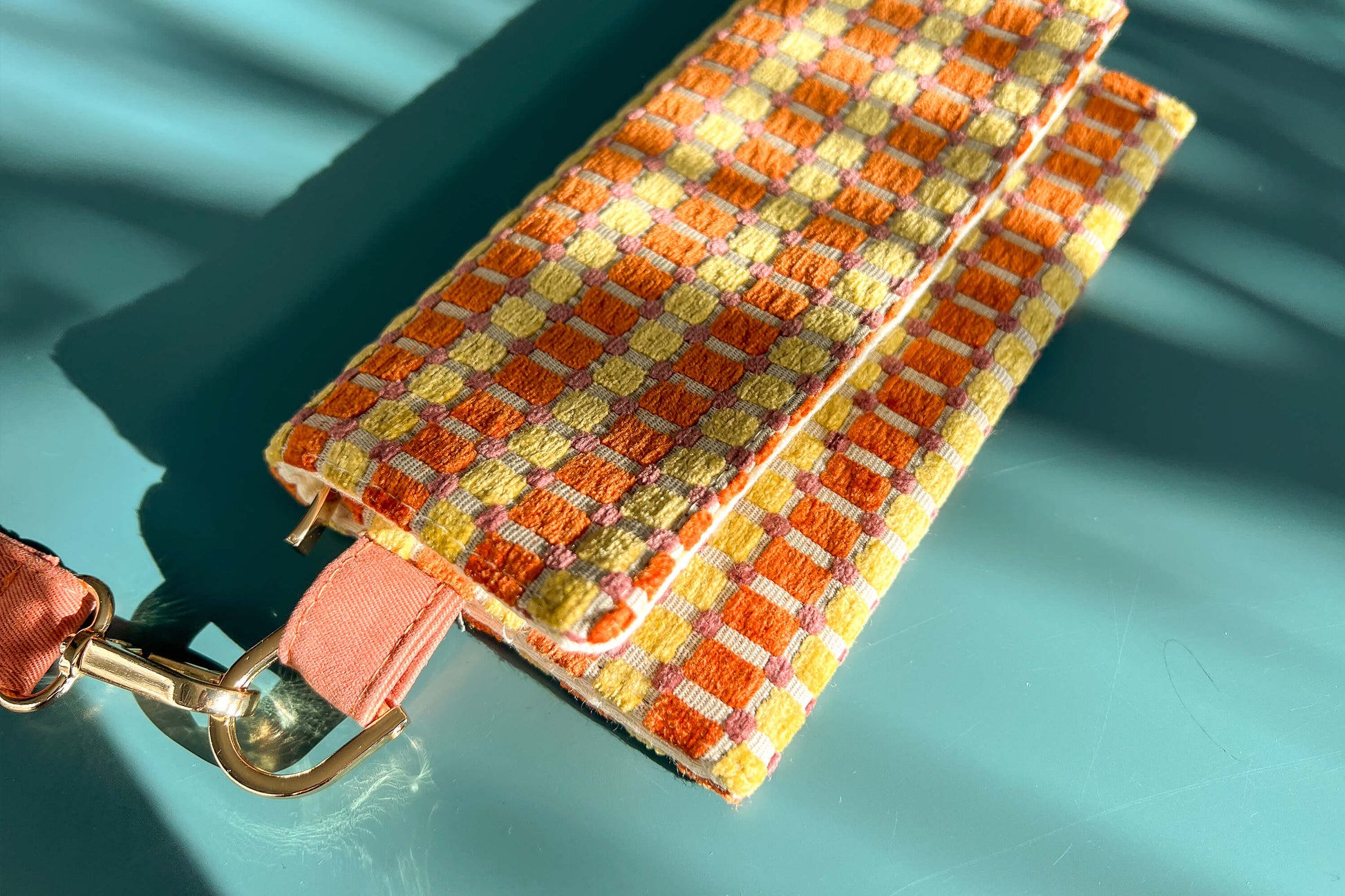 Detailansicht der Handtasche DANA in der Farbe gelb-orange-beige. Die Tasche liegt auf einem blauen Untergrund.