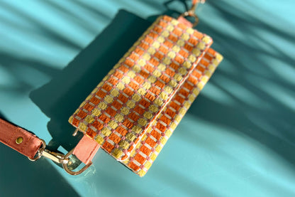 Gesamtansicht der Handtasche DANA in der Farbe gelb-orange-beige. Die Tasche liegt auf einem blauen Untergrund.