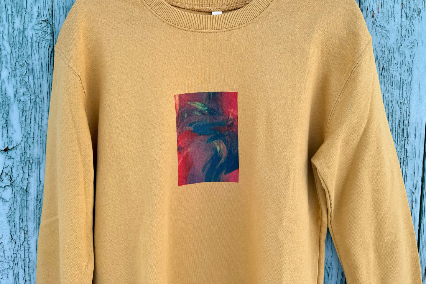 Detailansict von senffarbenem senffarbenes Unisex Sweatshirt mit rot-blau-gelb verlaufendem Druck von einem großen Rechteck auf der Brust, bedruckt mit Siebdruck. 